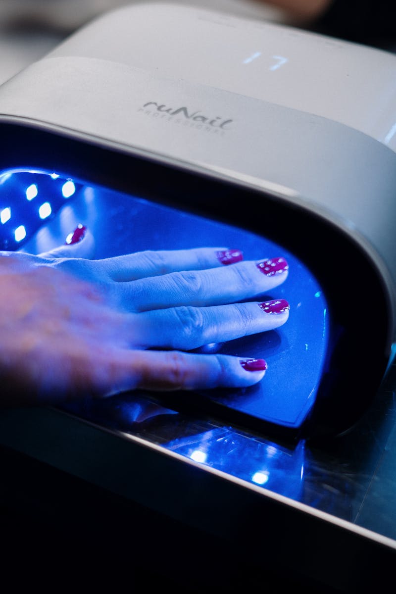 A hand with red nail art curing under a UV lamp in a professional nail salon.